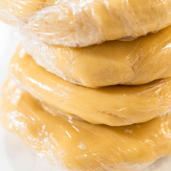 Tight shot of plastic-wrapped cookie dough, showing firm texture before rolling and cutting into shapes.