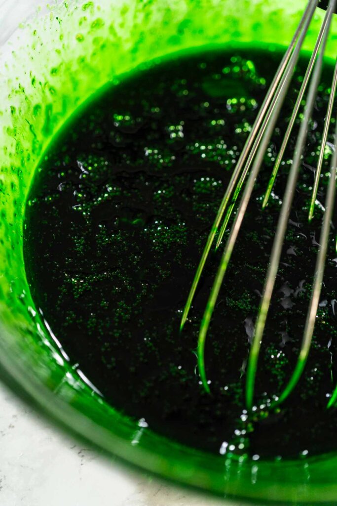 Close-up of a vibrant green mixture of food coloring and maple syrup in a bowl, ready to be blended into the cookie dough for Vibrant Green Gingerbread Cookies for Festive Baking.