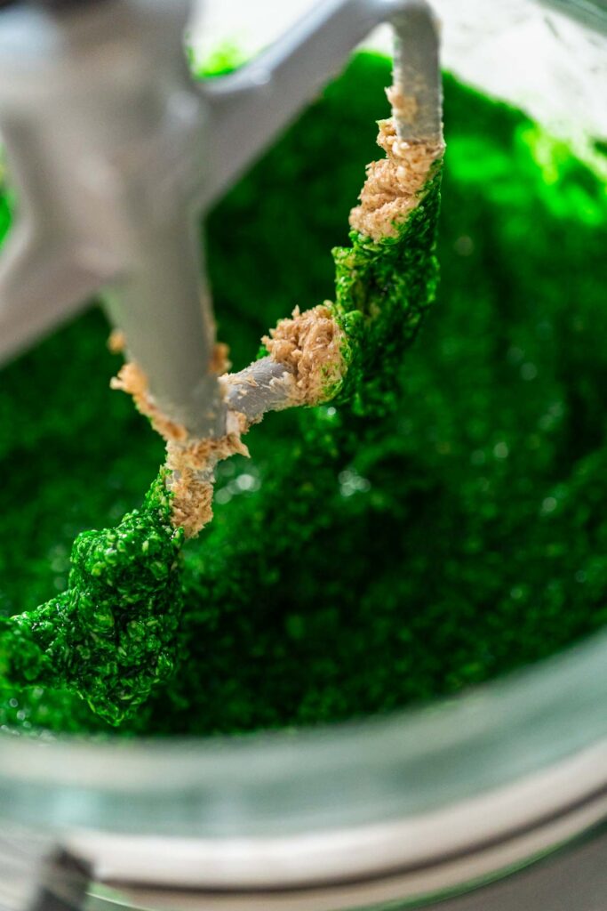 The vibrant green dough mixture for Vibrant Green Gingerbread Cookies for Festive Baking is starting to form, combining butter, sugar, and the green-tinted maple syrup in a mixer.