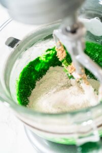 Dry ingredients added to the green mixture in the mixer to complete the dough for Vibrant Green Gingerbread Cookies for Festive Baking. The flour, spices, and green blend create a festive dough.