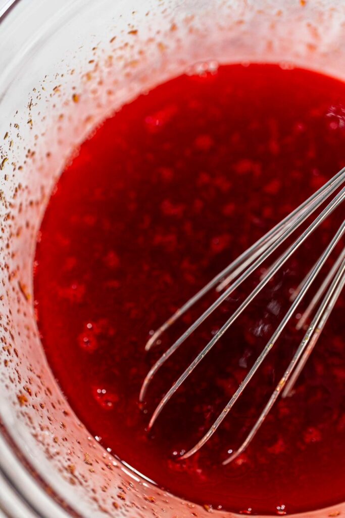 The molasses and egg mixture is being whisked together, creating a smooth, uniform consistency. The dark, rich color of the molasses will contribute to the dough’s distinctive red hue.