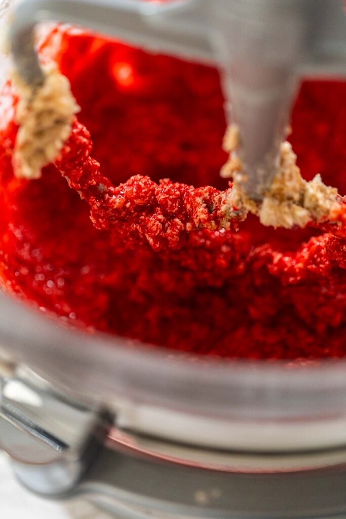 The maple syrup and egg mixture is added to the creamed butter and brown sugar in the mixing bowl. The wet ingredients blend together to create a vibrant base for the Classic Red Gingerbread Dough.