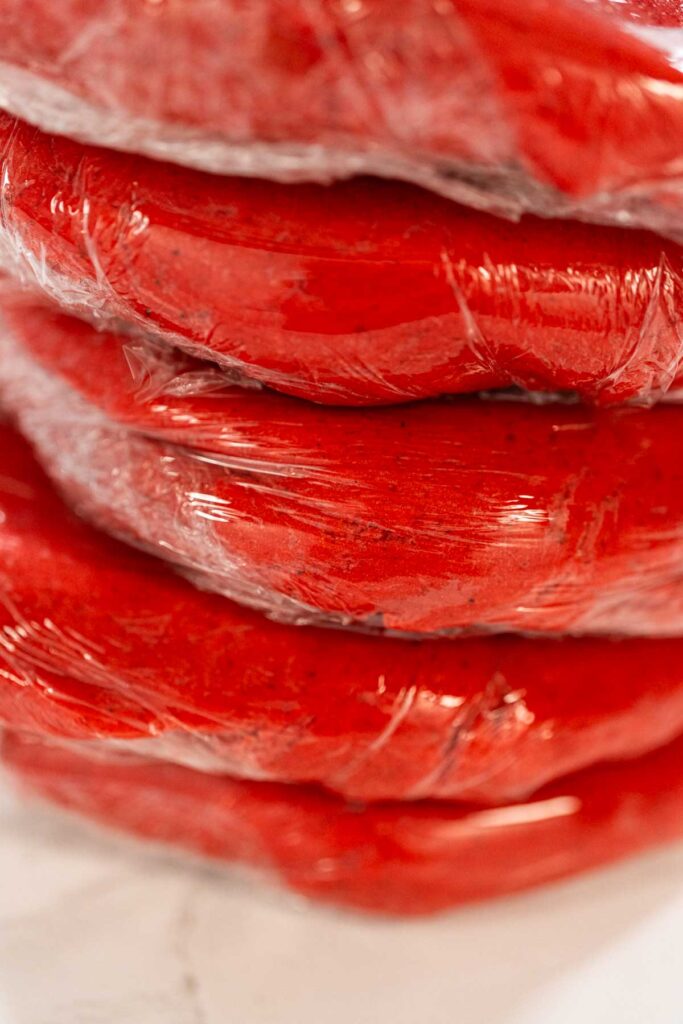Four portions of the Classic Red Gingerbread Dough, each wrapped in plastic, are stacked and ready for refrigeration. This step allows the dough to rest and develop flavor before baking.