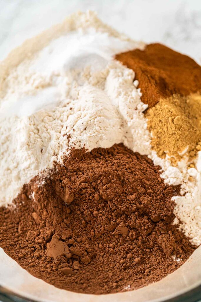 Close-up of a mixing bowl with cocoa powder, flour, ginger, and cinnamon for the Chocolate Ginger Sugar Cookie Dough, showing the spices and dry ingredients ready for mixing.