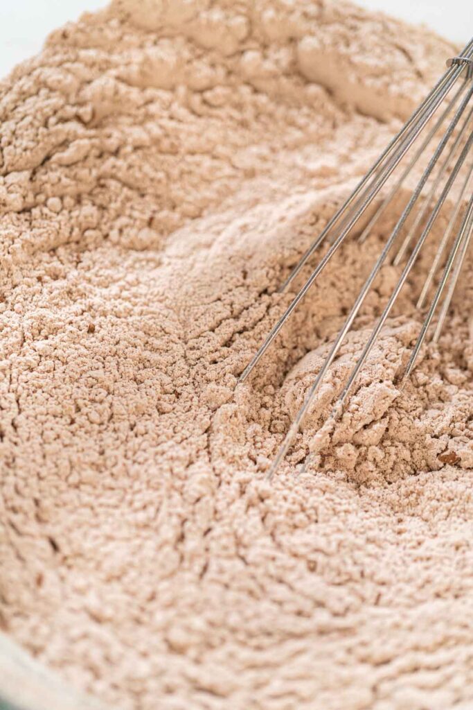 Close-up of a mixing bowl with cocoa powder, flour, ginger, and cinnamon for the Chocolate Ginger Sugar Cookie Dough, showing the spices and dry ingredients ready for mixing.