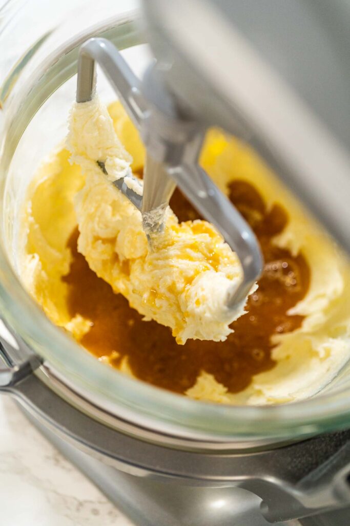 Close-up view of the stand mixer as maple syrup is added to the creamed butter and sugar mixture, forming the base for Chocolate Ginger Sugar Cookie Dough.