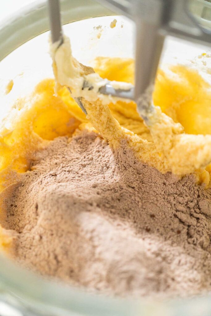 Dry ingredients, including flour and cocoa, added to the wet mixture in the stand mixer for Chocolate Ginger Sugar Cookie Dough, ready for final mixing.