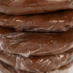 Stacked discs of Chocolate Ginger Sugar Cookie Dough wrapped in plastic, ready to chill, showing a smooth and uniform dough texture.