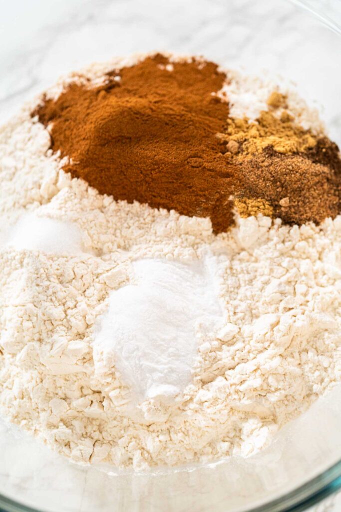 A close-up of a large mixing bowl holding dry ingredients for Spiced Gingerbread Cookie Dough Perfect for Baking. The bowl contains flour, baking soda, cinnamon, ginger, and cloves in neat sections, ready to be whisked together.