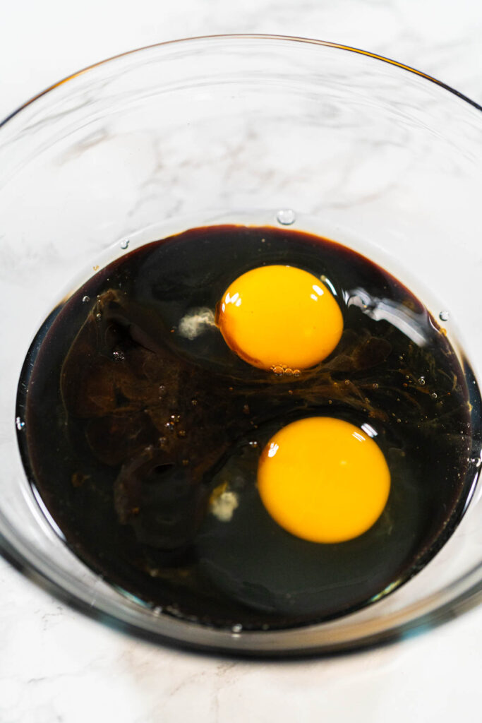 A bowl filled with molasses and two large eggs for Spiced Gingerbread Cookie Dough Perfect for Baking. The dark molasses contrasts with the bright yolks, creating a rich base for the dough.