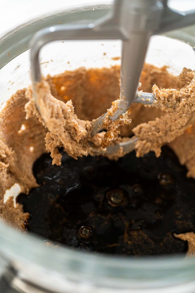 Close-up of molasses being added to the creamed butter and sugar mixture for Spiced Gingerbread Cookie Dough Perfect for Baking. The dark molasses contrasts with the light dough, creating a rich, dark color essential for gingerbread.