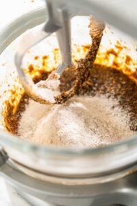 Close-up of dry ingredients being gradually incorporated into the molasses mixture in the stand mixer for Spiced Gingerbread Cookie Dough Perfect for Baking. The flour and spices create a balanced, flavorful dough.