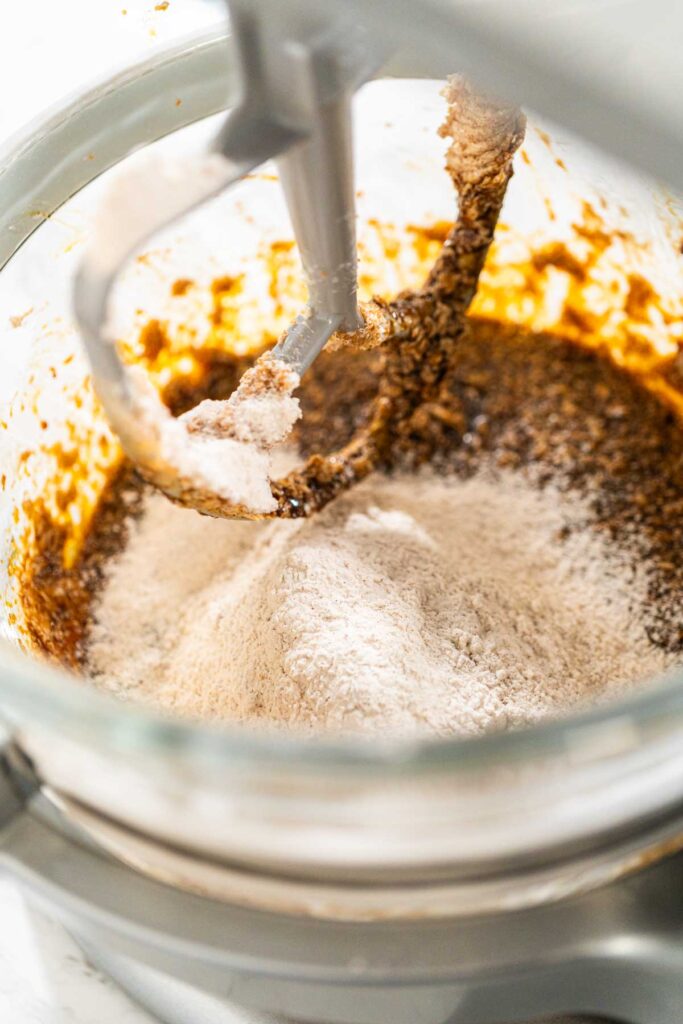 Close-up of dry ingredients being gradually incorporated into the molasses mixture in the stand mixer for Spiced Gingerbread Cookie Dough Perfect for Baking. The flour and spices create a balanced, flavorful dough.