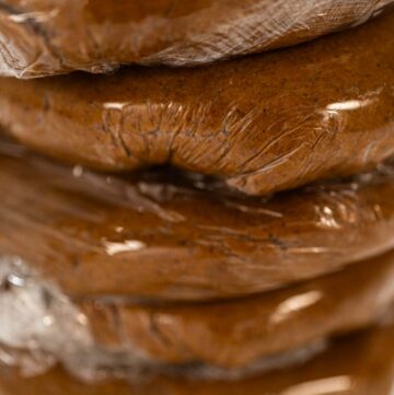 Stacked portions of Spiced Gingerbread Cookie Dough Perfect for Baking wrapped in plastic wrap. The dough is divided for easy handling and chilled, ready for rolling and shaping into cookies.