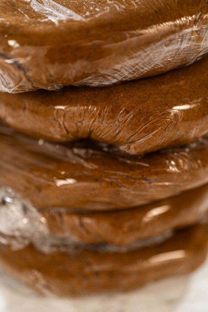 Stacked portions of Spiced Gingerbread Cookie Dough Perfect for Baking wrapped in plastic wrap. The dough is divided for easy handling and chilled, ready for rolling and shaping into cookies.