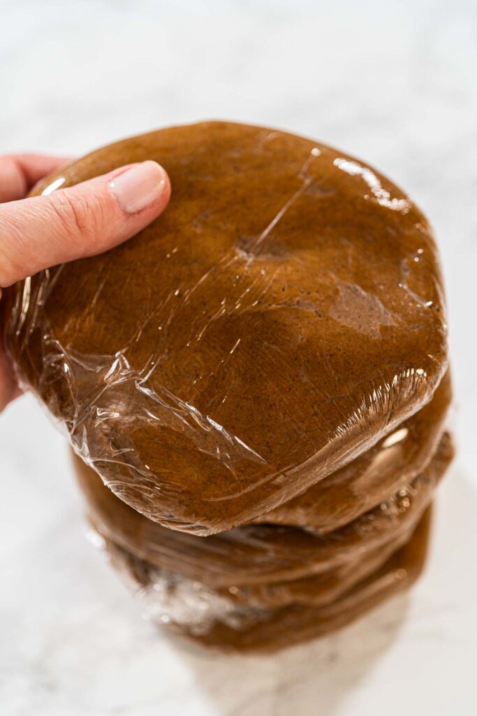 Stacked portions of Spiced Gingerbread Cookie Dough Perfect for Baking wrapped in plastic wrap. The dough is divided for easy handling and chilled, ready for rolling and shaping into cookies.