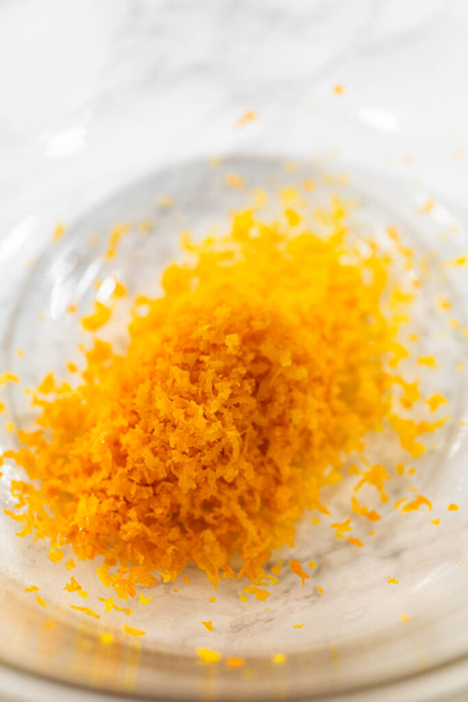 A close-up of bright orange zest in a glass bowl, which will add a zesty flavor to the Zesty Orange Gingerbread Cookie Dough. This fresh zest is key to enhancing the dough’s citrusy undertone.