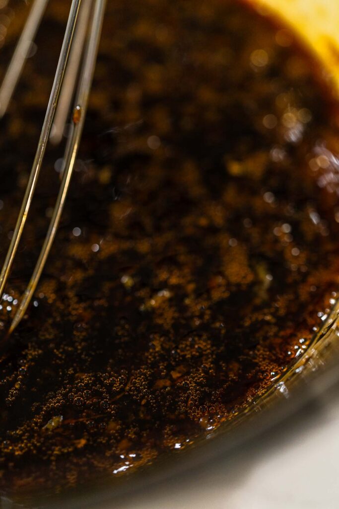 Molasses, eggs, and orange zest whisked together in a glass bowl for Zesty Orange Gingerbread Cookie Dough. The mixture has a rich, dark color with flecks of bright orange zest, creating a balanced flavor profile.