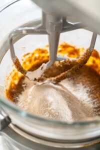 Dry ingredients gradually added to the wet mixture in the stand mixer for Zesty Orange Gingerbread Cookie Dough. Flour and spices are incorporated for a balanced, spiced dough texture.