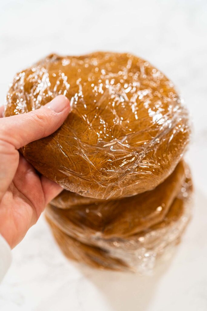 Portions of Zesty Orange Gingerbread Cookie Dough wrapped in plastic wrap and stacked, ready for chilling. Dividing the dough ensures easier handling when rolling out and cutting shapes later.