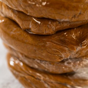 Portions of Zesty Orange Gingerbread Cookie Dough wrapped in plastic wrap and stacked, ready for chilling. Dividing the dough ensures easier handling when rolling out and cutting shapes later.