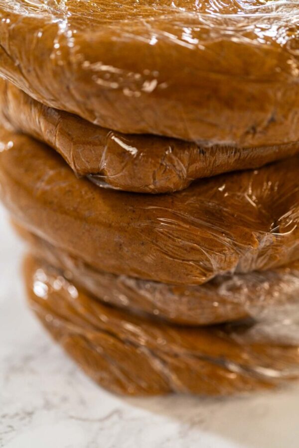 Portions of Zesty Orange Gingerbread Cookie Dough wrapped in plastic wrap and stacked, ready for chilling. Dividing the dough ensures easier handling when rolling out and cutting shapes later.