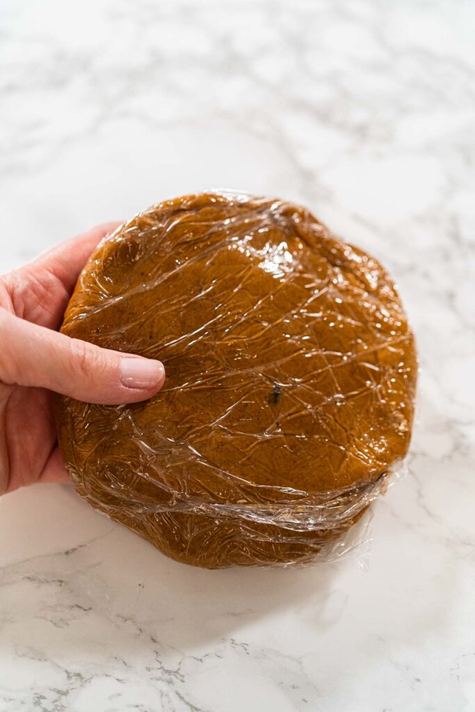 Close-up of a single portion of Zesty Orange Gingerbread Cookie Dough wrapped in plastic wrap, ready to be chilled. The smooth dough surface hints at a rich, flavorful result after baking.
