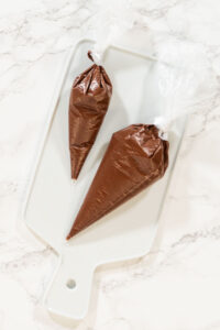 Piping Bags on Cooling Rack Description: Overhead view of piping bags filled with melted chocolate resting on a cooling rack, prepared for the Chocolate Royal Icing recipe.