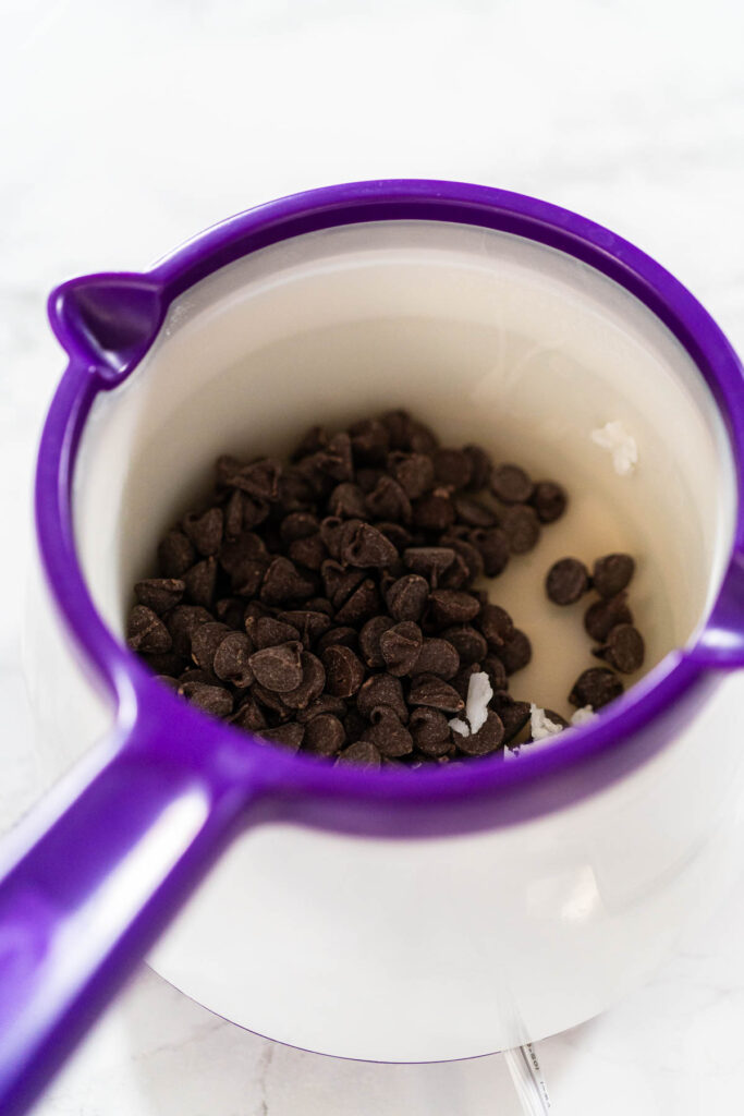 Chocolate Chips and Coconut Oil in Melting Pot Description: Overhead view of chocolate chips and coconut oil in a purple melting pot, prepared for melting into a smooth chocolate royal icing.