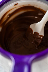 Melted Chocolate in Melting Pot with Spatula Description: Close-up view of melted chocolate being stirred with a spatula in a purple melting pot, achieving a smooth consistency for Chocolate Royal Icing.
