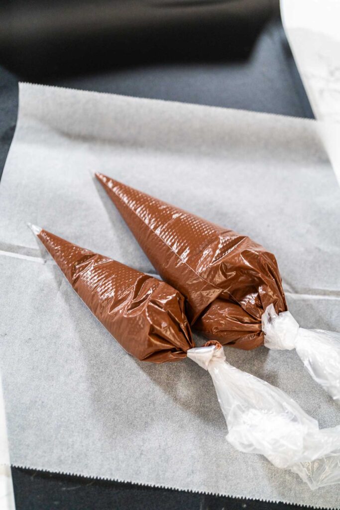Filled Piping Bags with Chocolate Icing Description: Close-up view of two piping bags filled with chocolate royal icing, placed on a white tray, prepared for decorating cookies.