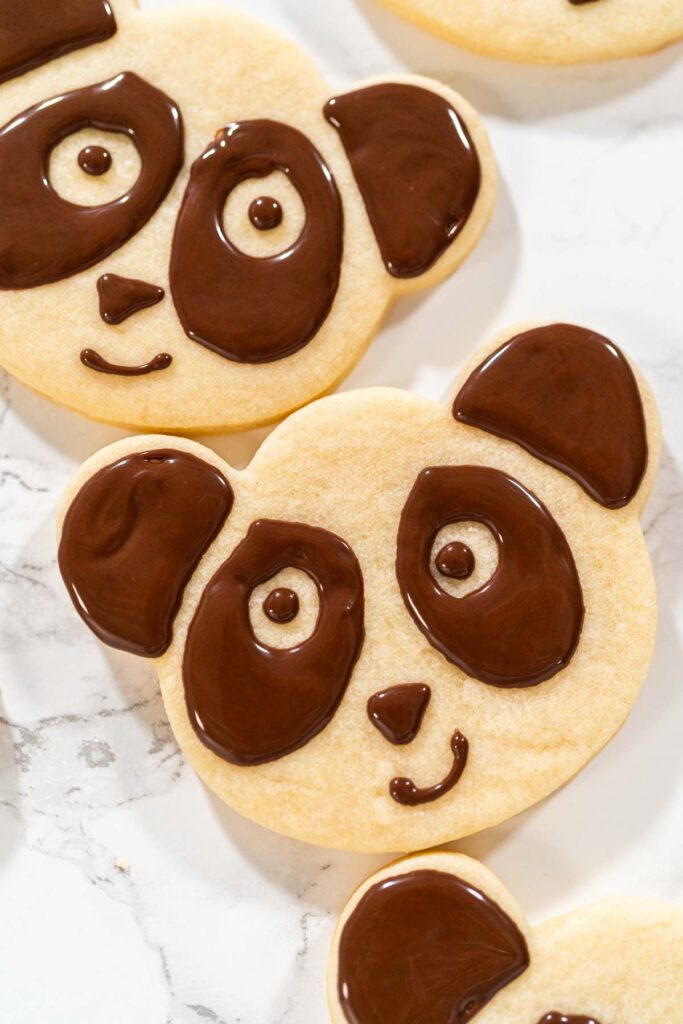 Overhead view of a batch of panda cookies with completed chocolate icing designs for the Chocolate Royal Icing Recipe. Each cookie features a cute panda face, giving a uniform and adorable look.
