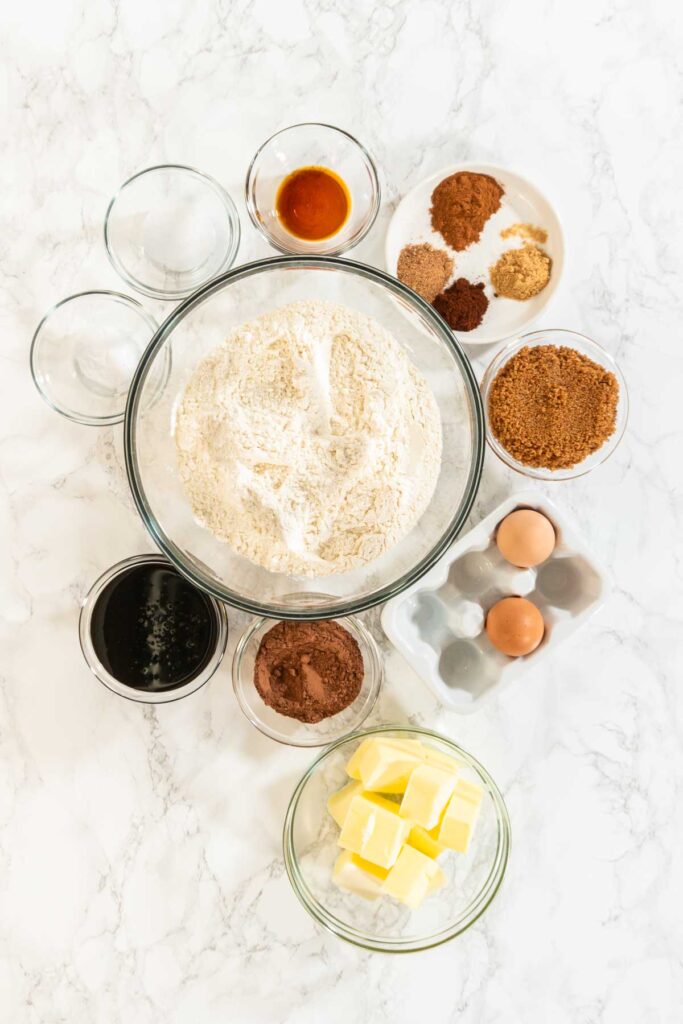 A beautiful arrangement of ingredients for Chocolate Gingerbread Cookie Dough, including flour, butter, brown sugar, molasses, eggs, and a variety of spices. These ingredients are essential for creating rich and festive holiday cookies.