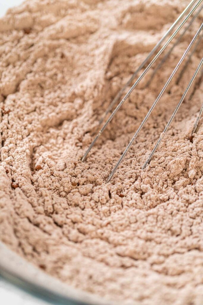 Mixing dry ingredients for Chocolate Gingerbread Cookie Dough, including flour, cocoa powder, cinnamon, ground ginger, and cloves in a glass bowl. The ingredients are layered and ready to be combined, creating a rich, aromatic base for the cookie dough.