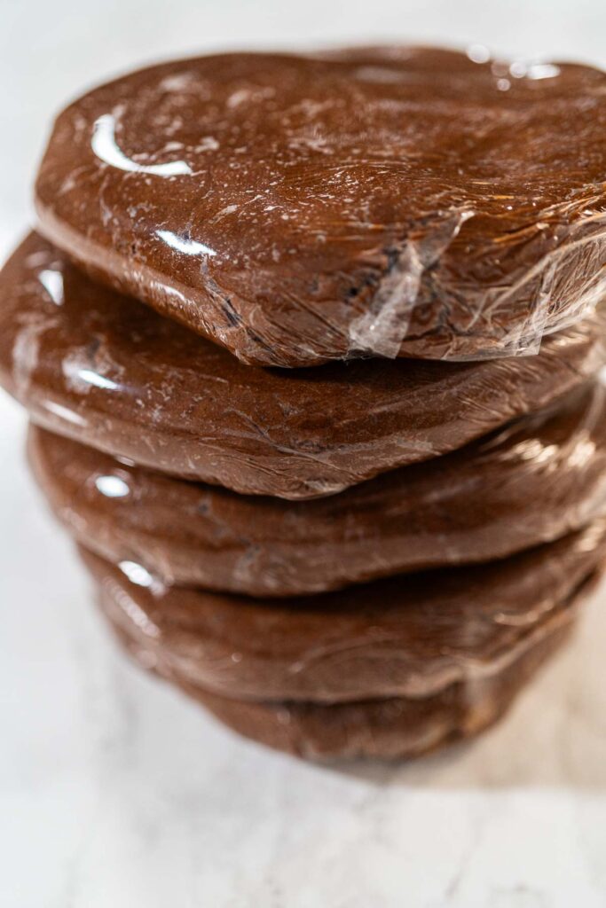 Multiple discs of Chocolate Gingerbread Cookie Dough wrapped in plastic wrap, stacked and ready to chill. These dough discs make it convenient to shape cookies for holiday baking.