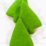 Three Green Gingerbread Cookies are arranged together in a standing formation, displaying their festive Christmas tree shape and vivid green color.