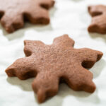 Close-up side view of a single baked Chocolate Ginger Sugar Cookie in the shape of a snowflake, resting on parchment paper.