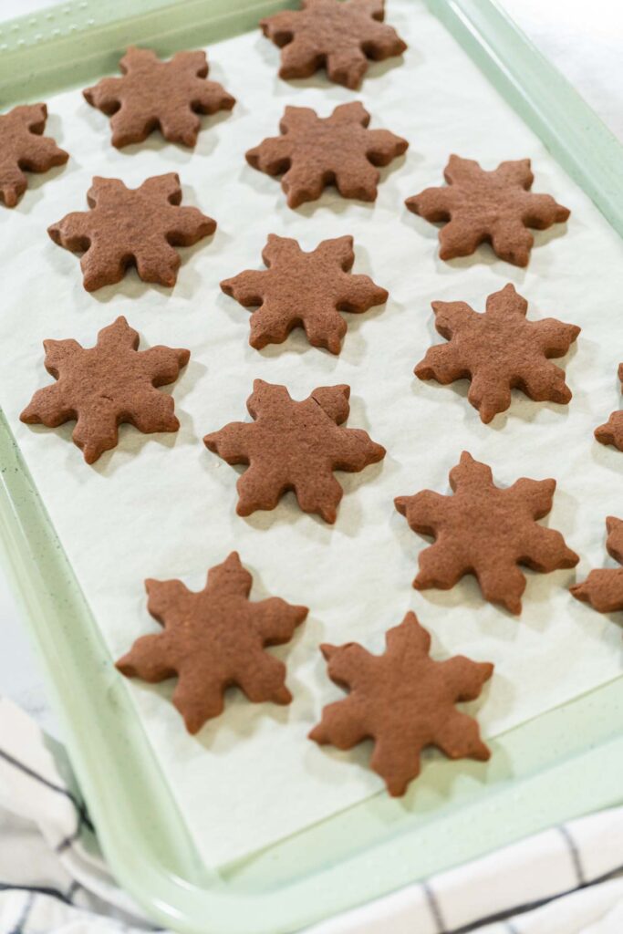 Chocolate Ginger Sugar Cookies in Snowflake Shapes A Festive Tre - Arina Photography Close-up side view of a single baked Chocolate Ginger Sugar Cookie in the shape of a snowflake, resting on parchment paper.
