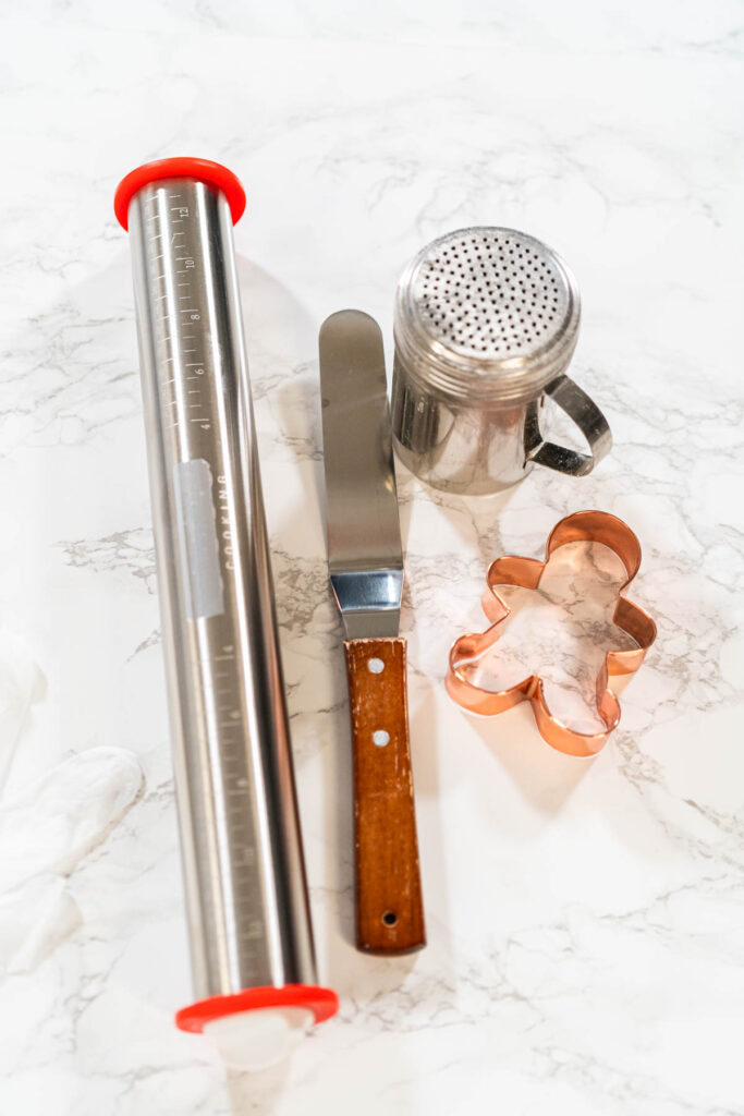Step-by-Step Process of Making Spiced Gingerbread Cookies - Arina Photography Straight-on view of baking tools, including a rolling pin, cookie cutters, and a sifter, placed on a marble countertop beside spiced gingerbread dough.