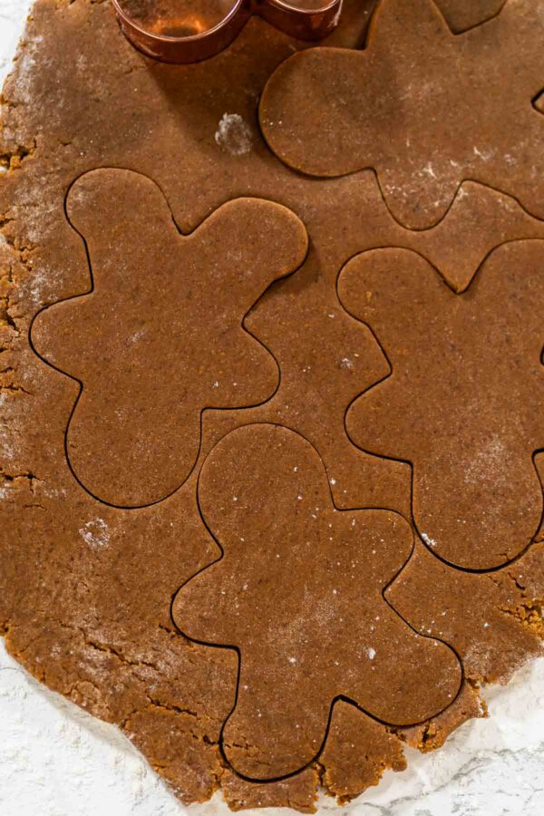 Eye-level view of gingerbread men-shaped cookie cutters pressed into rolled-out spiced gingerbread dough, showing the shaping process.