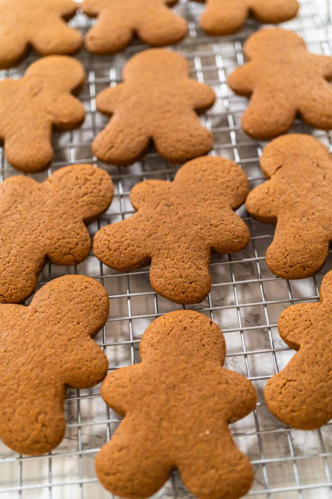 Step-by-Step Process of Making Spiced Gingerbread Cookies - Arina Photography Close-up view of a tray of freshly baked gingerbread man cookies placed on a cooling rack, highlighting festive details.