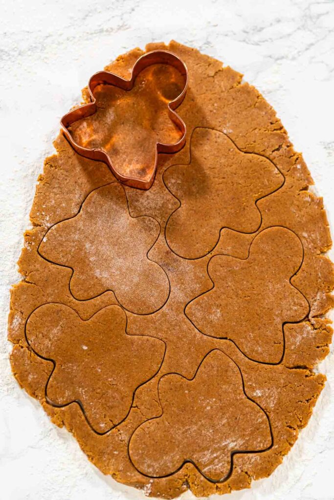 The entire dough sheet is filled with gingerbread girl shapes, ready to be transferred to the baking tray. Captured from a top-down perspective.