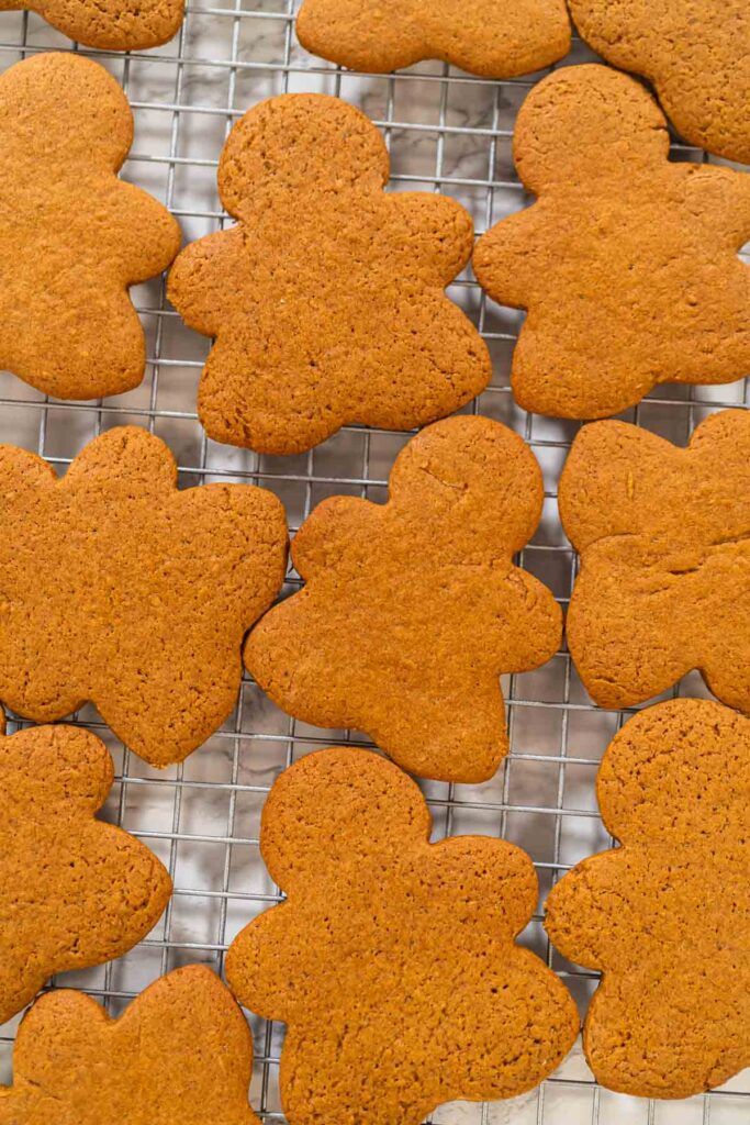 Freshly baked Orange Zest Gingerbread Cookies in gingerbread girl shapes cooling on a wire rack, viewed from an angled perspective.