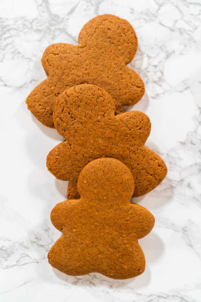 A stack of Orange Zest Gingerbread Cookies in gingerbread girl shapes on a white surface, showcasing their festive design and uniform texture.