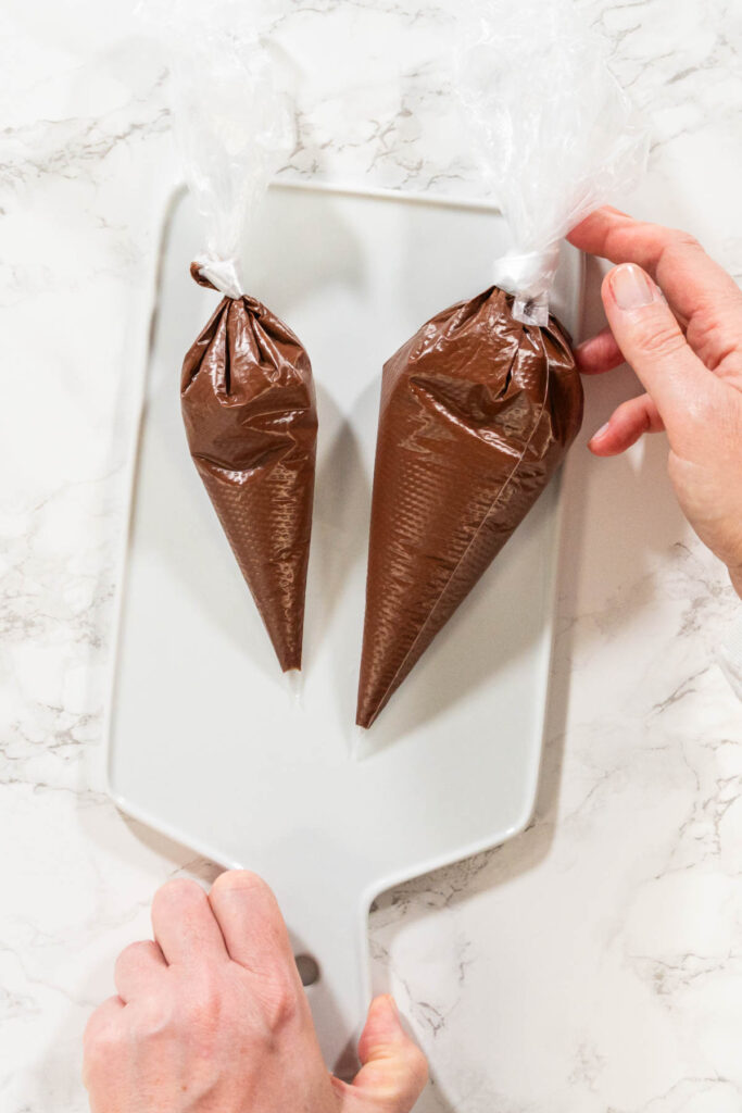 Piping Bags on Cooling Rack Description: Overhead view of piping bags filled with melted chocolate resting on a cooling rack, prepared for the Chocolate Royal Icing recipe.