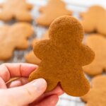 Preparing and Baking Classic Gingerbread Cookies in Gingerbread - Arina Photography Close-up of a hand holding a baked gingerbread man cookie over a cooling rack filled with cookies.