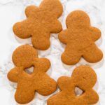 A hand holding a gingerbread man cookie with a heart-shaped cutout, close-up view.