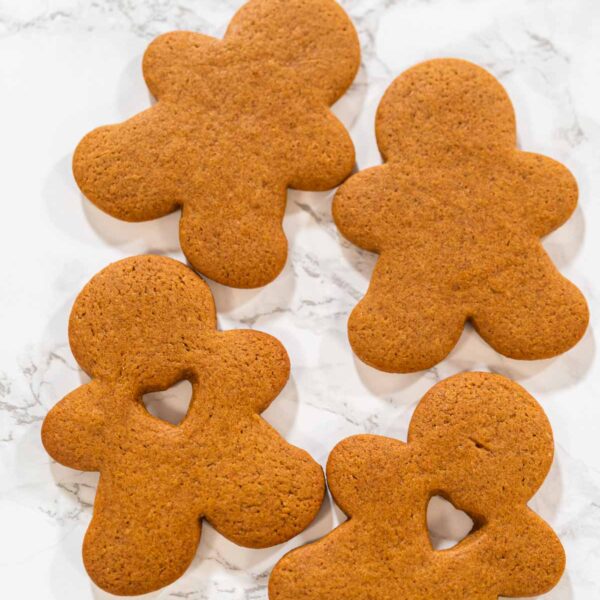 A hand holding a gingerbread man cookie with a heart-shaped cutout, close-up view.