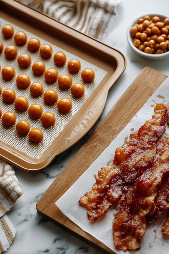 Round caramel candies lined neatly on a silicone mat with bacon in the background.