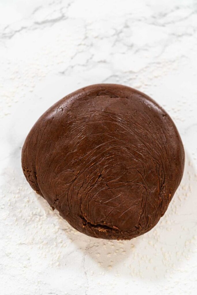 Ball of chocolate-spiced gingerbread cookie dough on a floured marble surface ready for rolling.